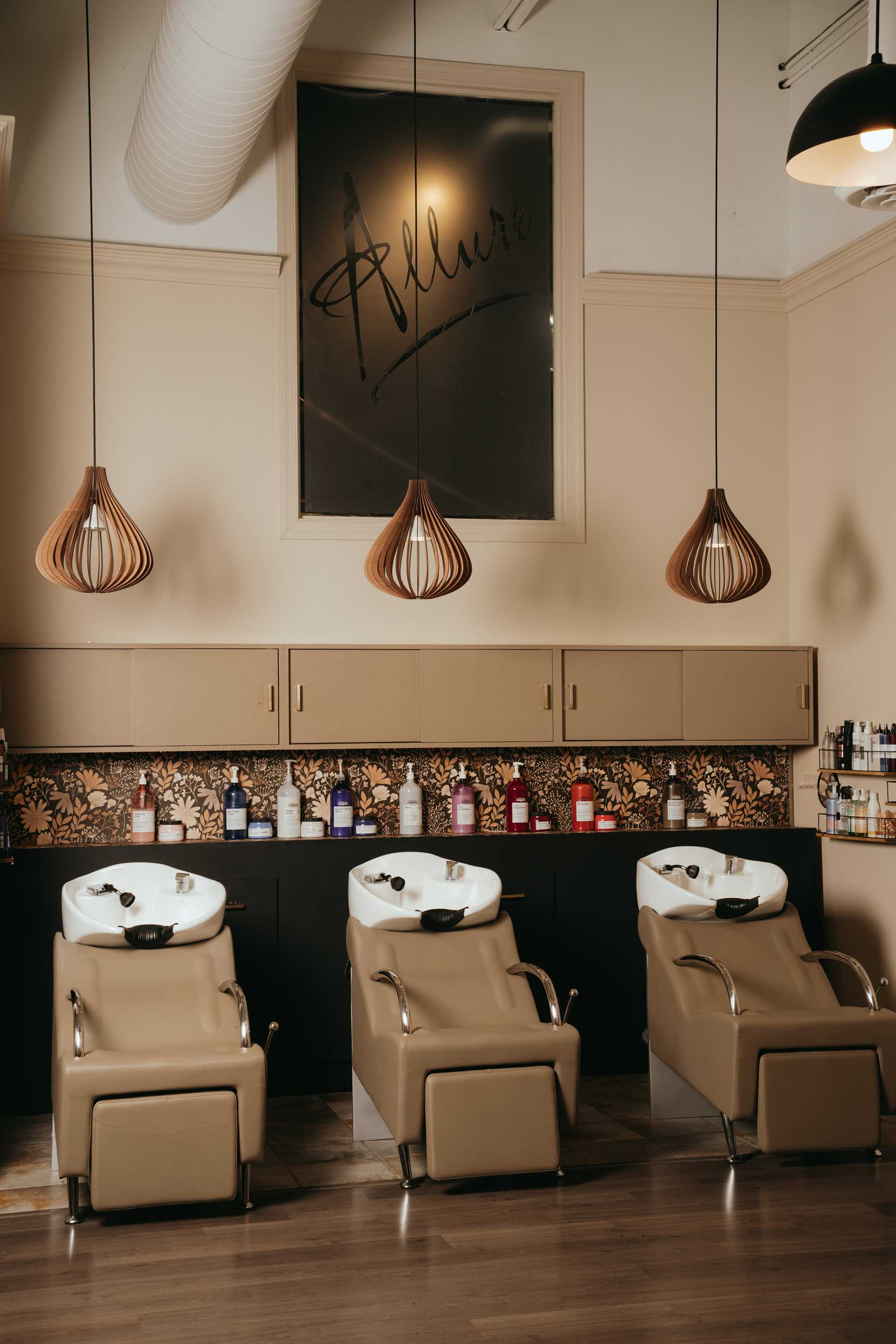 Three salon washing stations with brown chairs under elegant pendant lights.