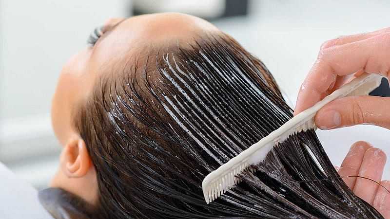 Applying hair treatment with a comb to a person's scalp in a salon.