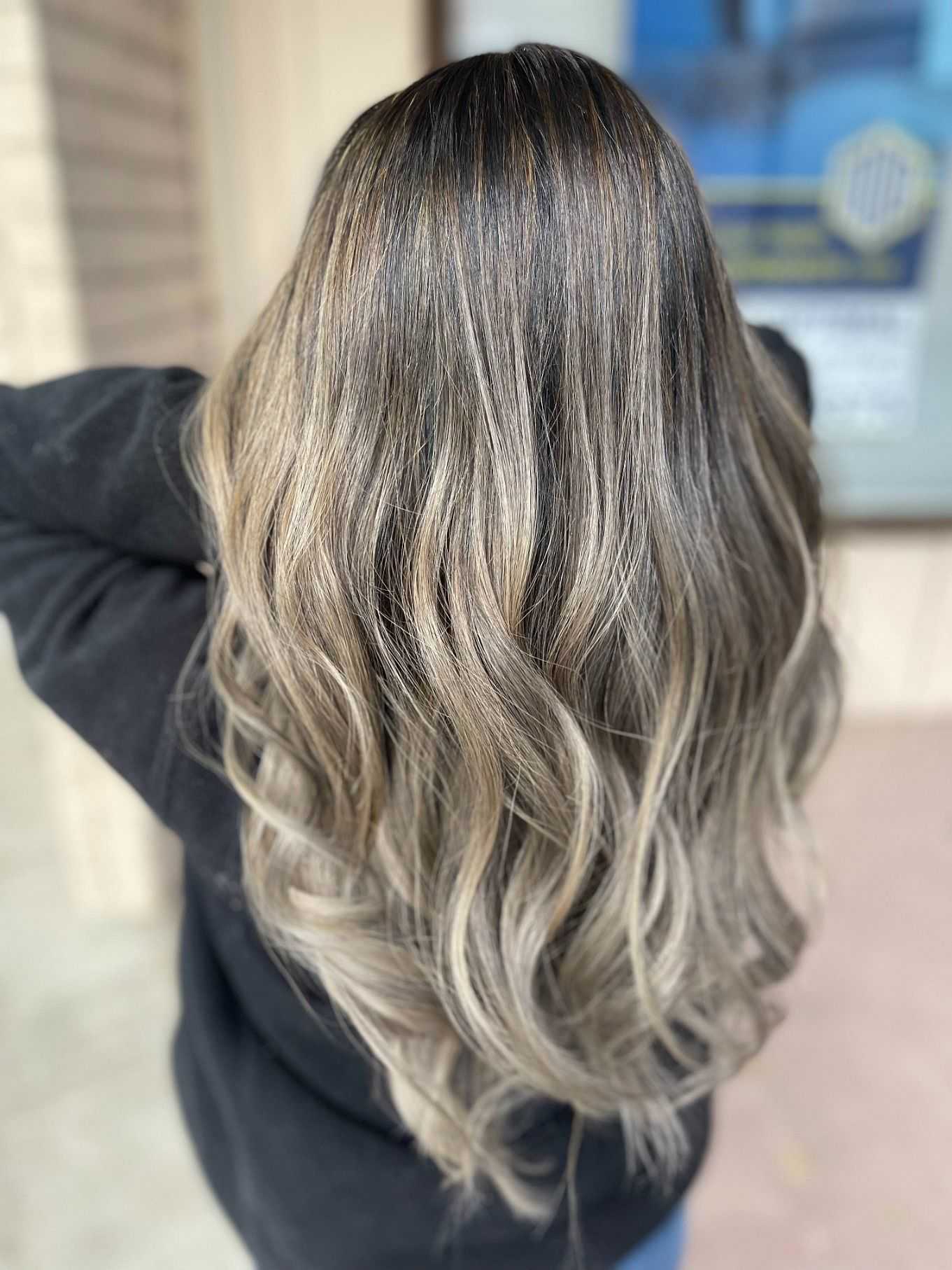 Person with long, wavy, brown and blonde highlighted hair, viewed from the back.