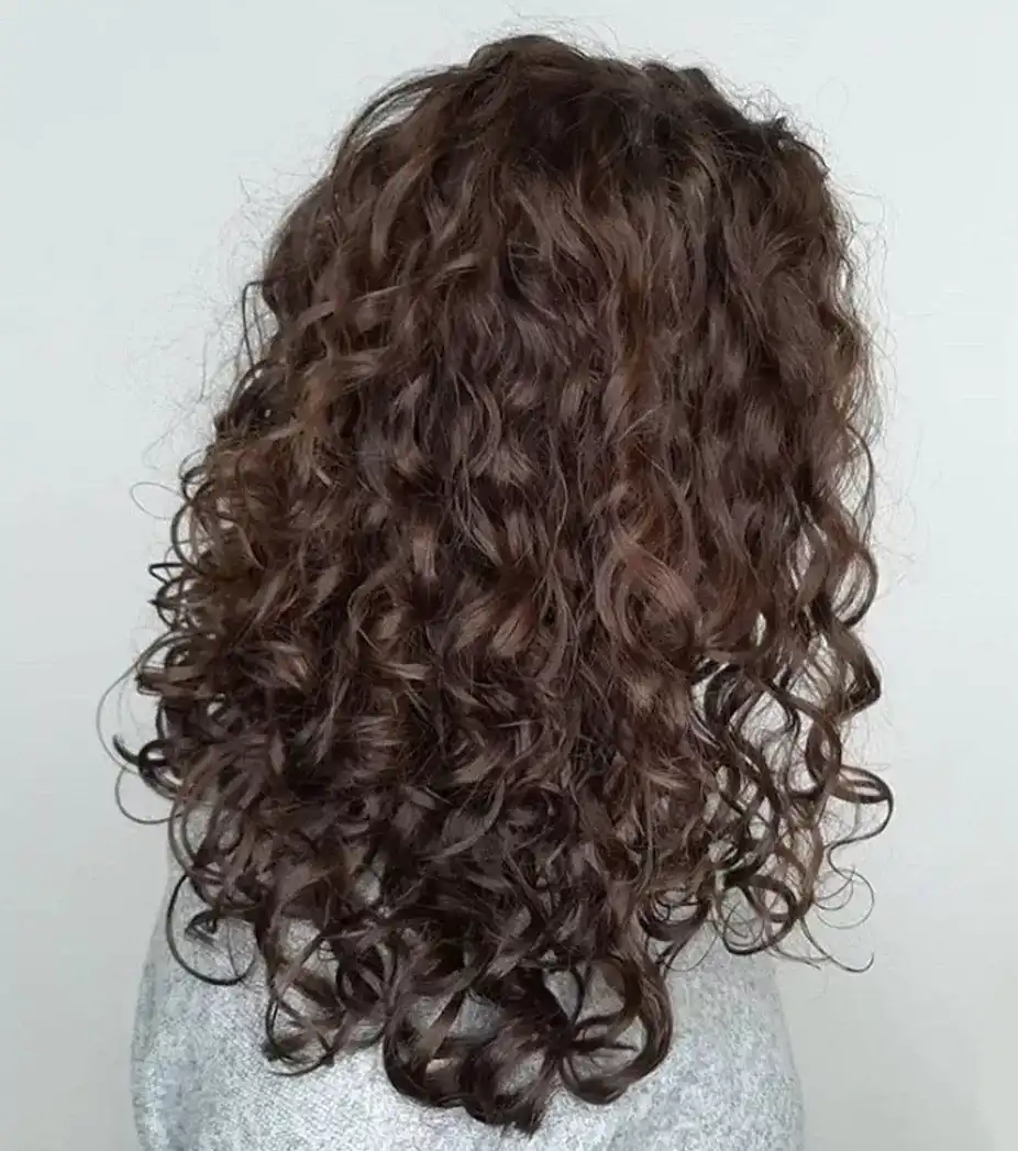 Curly brown hair cascading over a light gray sweater.